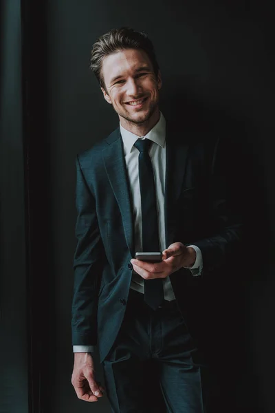 Cintura hacia arriba del hombre alegre y elegante sonriendo y sosteniendo el teléfono inteligente — Foto de Stock