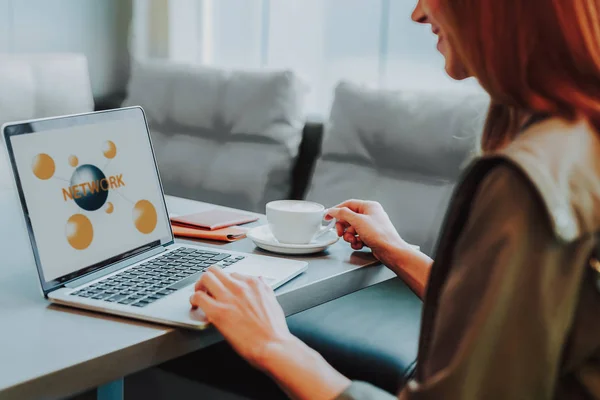 Grinande kvinna nätverk på laptop med varm dryck — Stockfoto