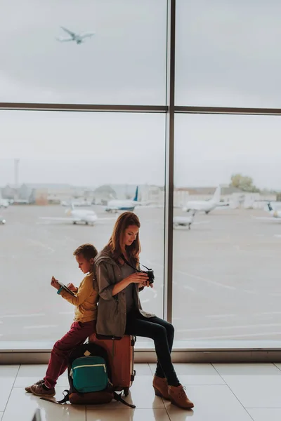 Moeder en zoon maken gebruik van gadgets tijdens het wachten voor vliegtuig — Stockfoto