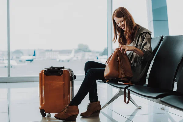 Mujer sonriente espera vuelo con maleta —  Fotos de Stock