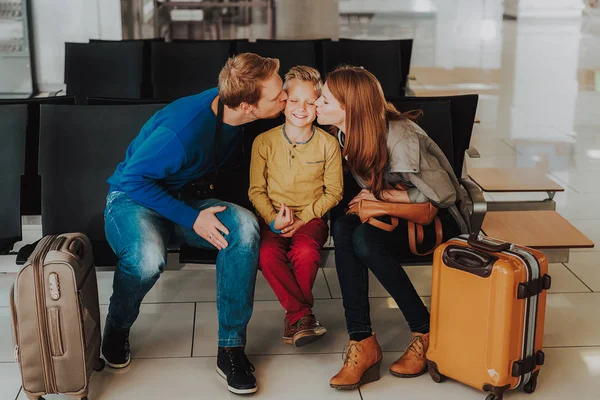 Delighted kid is being kissed by parents at airport — Stock Photo, Image