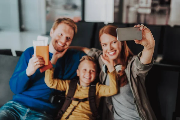 Smiling parents with boy are taking selfie at airport