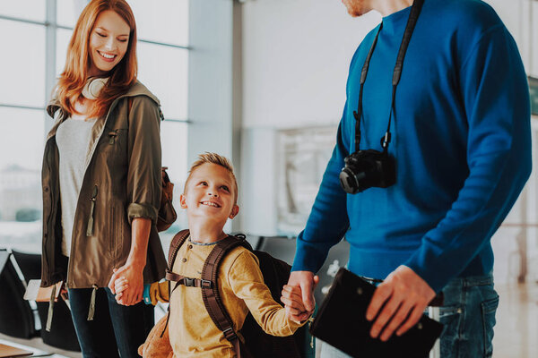 Cheerful couple is taking son by hands before flight