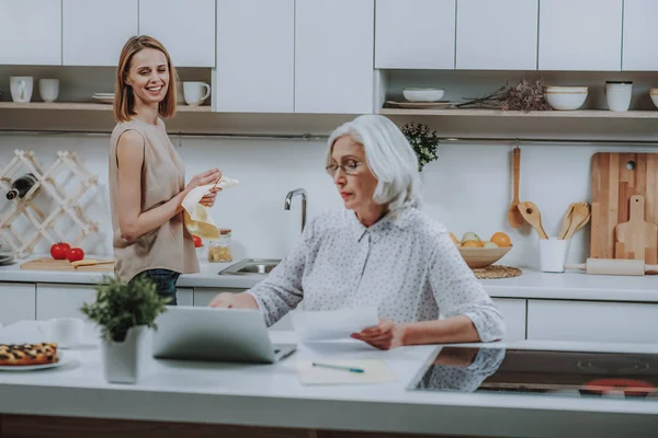 Feliz hembra está observando a su madre con un cuaderno en la cocina — Foto de Stock