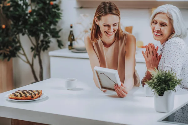 La hija feliz con la mamá admiran la foto en la cocina — Foto de Stock