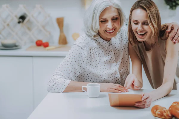 Зрелые и молодые женщины смеются во время просмотра фотографий в помещении — стоковое фото
