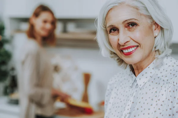 Mujer anciana sonriente es relajante mientras su hija está cocinando — Foto de Stock