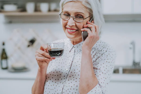 Fröhliche alte Frau plaudert am Telefon mit Heißgetränk — Stockfoto