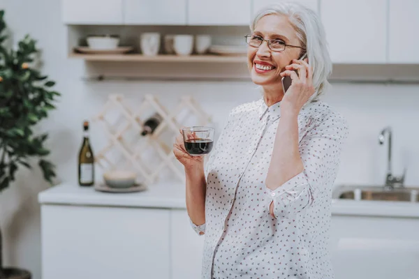 Веселая зрелая женщина пьет кофе, разговаривая по телефону — стоковое фото