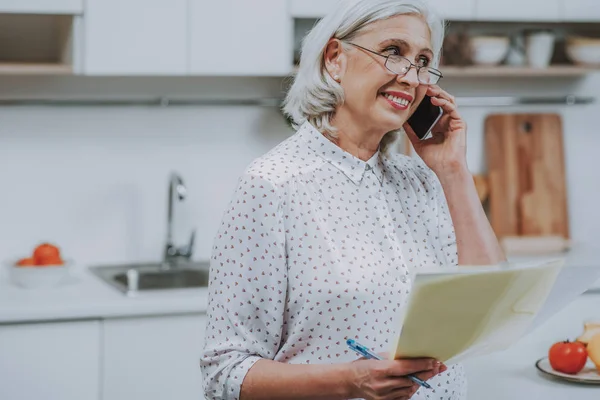 Mujer anciana sonriente se está comunicando por teléfono en casa —  Fotos de Stock