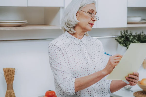 Mujer de pelo gris envejecido está escribiendo en la cocina — Foto de Stock