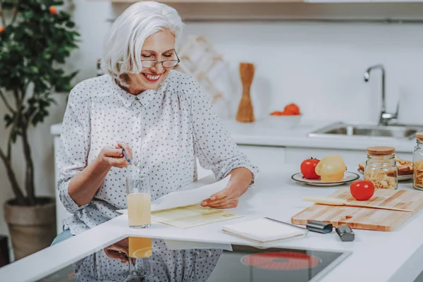 Fröhliche alte Dame liest Rezept, bevor sie zu Hause kocht — Stockfoto