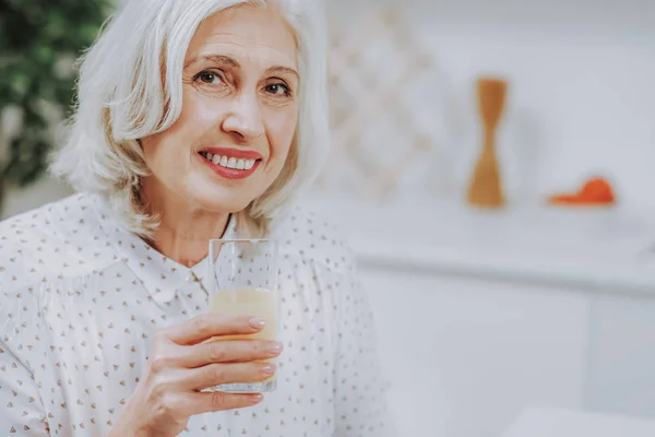 Счастливая старшая леди наслаждается свежим напитком в помещении — стоковое фото
