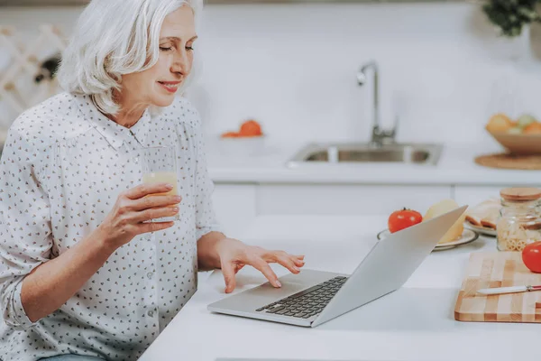 Freudige alte Dame entspannt mit Drink und Notizbuch drinnen — Stockfoto