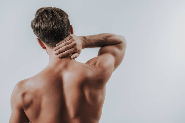 Shirtless young man standing and touching his neck