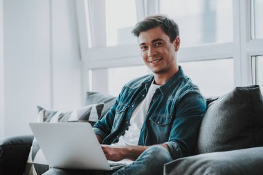 Dizüstü bilgisayar ile kanepede otururken gülümseyen rahat adam