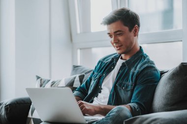 Kanepede oturan ve modern dizüstü holding neşeli adam