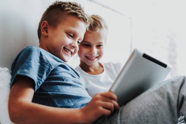 Mutlu çocuklar yatakta dijital tablet ile oturan