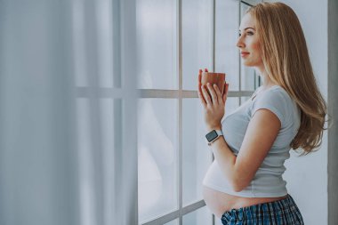 Gelecekte anne pencere yanında içecek ile ayakta gülümseyen.