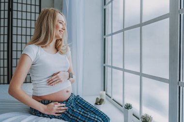 Evde koltukta oturan hamile bayan gülüyor