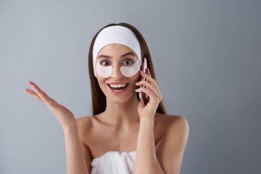 Excited young lady with under-eye patches talking on cellphone clipart