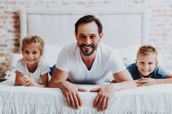 Padre alegre y dos niños acostados en la cama — Foto de Stock