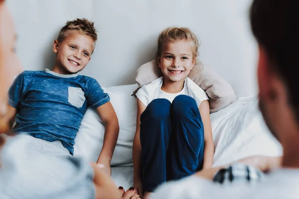 Feliz dos niños sentados en la cama delante de los padres — Foto de Stock