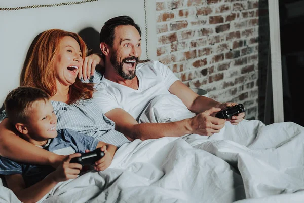 Familia feliz acostado en la cama y jugar juegos —  Fotos de Stock