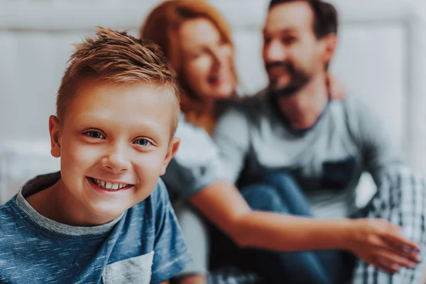 Gelukkig lachend jongen zittend met ouders op bed — Stockfoto