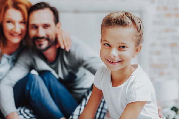 Feliz chica sonriente sentada con los padres en la cama — Foto de Stock