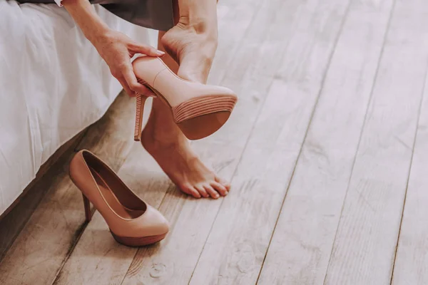 Frazzling young woman unshoes stilletos from feet at home — Stock Photo, Image