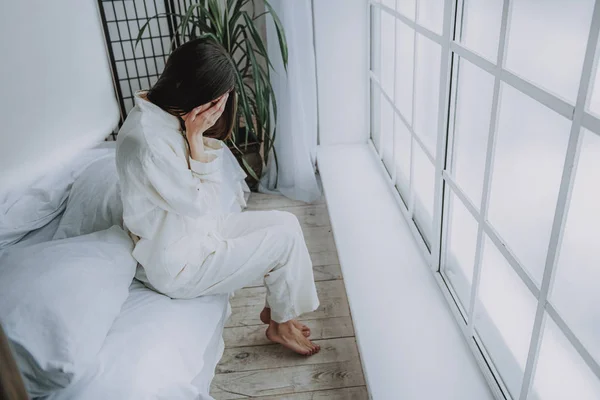 Przygnębiony asian kobieta siedzi na łóżku obok szerokości okna — Zdjęcie stockowe