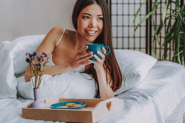 Sonriente joven hembra degustación de bebidas en la cama en casa —  Fotos de Stock