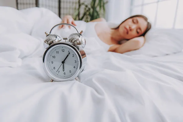 Relógio de alarme localizando na frente da jovem mulher na cama — Fotografia de Stock