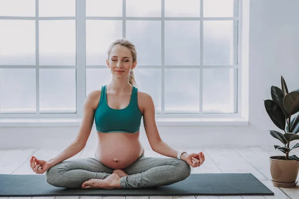 Hermosa joven embarazada meditando en alfombra deportiva — Foto de Stock
