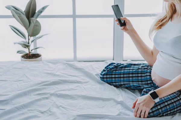 Молода майбутня мати використовує мобільний телефон у своїй спальні — стокове фото