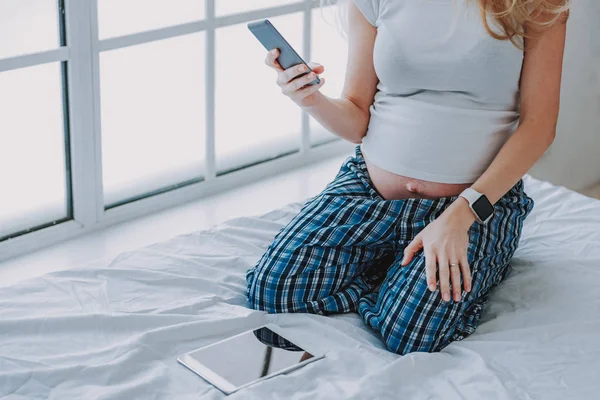 Senhora expectante segurando telefone celular na cama — Fotografia de Stock