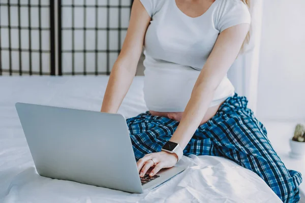 Mulher grávida usando laptop na cama enquanto descansa no quarto — Fotografia de Stock