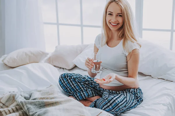 Smiling pregnant woman with glass of water and vitamin pills on bed — Stock Photo, Image