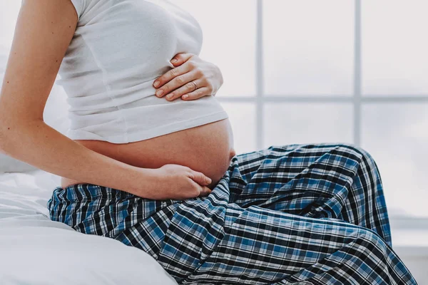 Terhes hölgy pizsamában megható neki pocakját, világos hálószoba — Stock Fotó