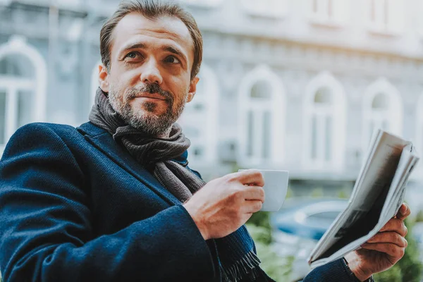 Позитивный мужчина пьет горячий напиток и читает газету на улице. — стоковое фото