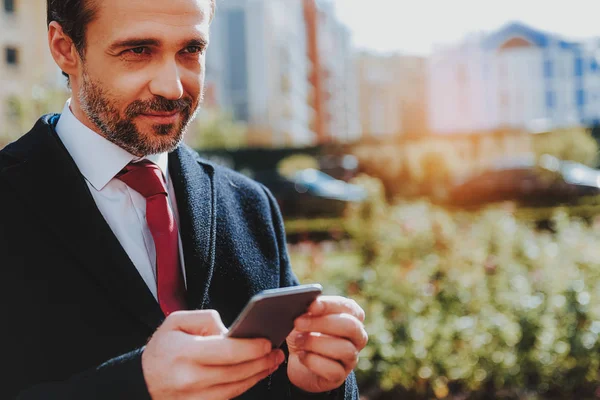 Positivo uomo d'affari in cappotto nero sta usando il telefono fuori — Foto Stock