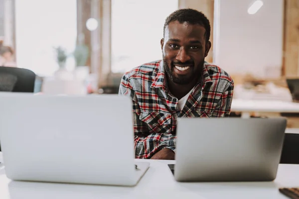 Positieve Afro-Amerikaanse man lachend en met behulp van twee moderne laptops — Stockfoto