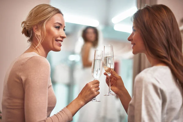 Senhoras sorridentes sentadas no showroom com champanhe — Fotografia de Stock