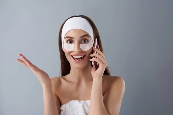 Excited young lady with under-eye patches talking on cellphone — Stock Photo, Image