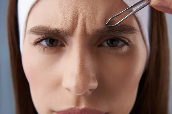 Mujer joven enojada arrancando cejas con pinzas —  Fotos de Stock