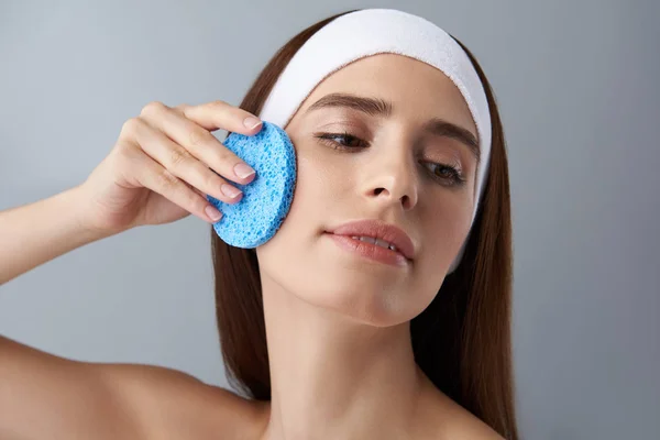 Okouzlující mladá dáma v čištění obličeje bílá čelenka s modrá houba — Stock fotografie