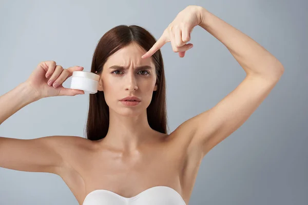 Geërgerd jonge vrouw met cosmetisch product waaruit blijkt huidproblemen op haar voorhoofd — Stockfoto