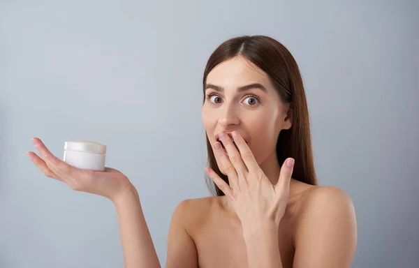 Förvånad ung dam med kosmetisk produkt som täcker hennes vidöppna mun med hand — Stockfoto