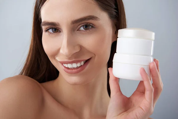 Attraktive junge Frau mit perfekter Haut zeigt Kosmetikprodukte — Stockfoto